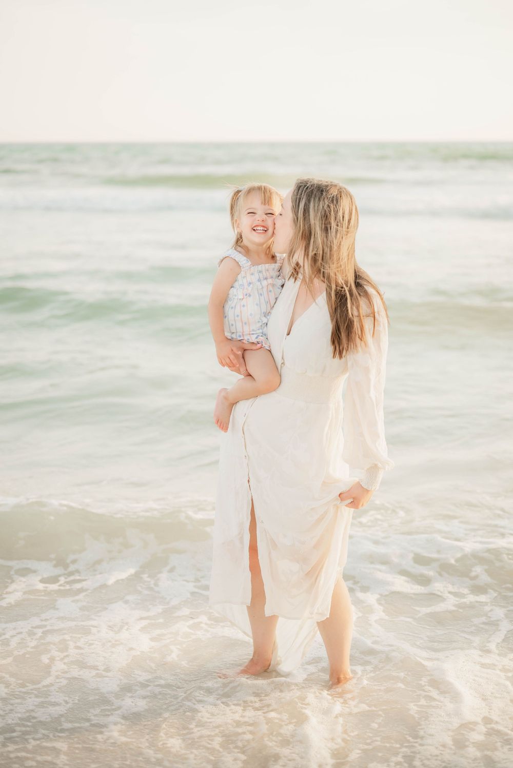 A tender moment shared between parent and child while standing in gentle ocean waves at the beach.