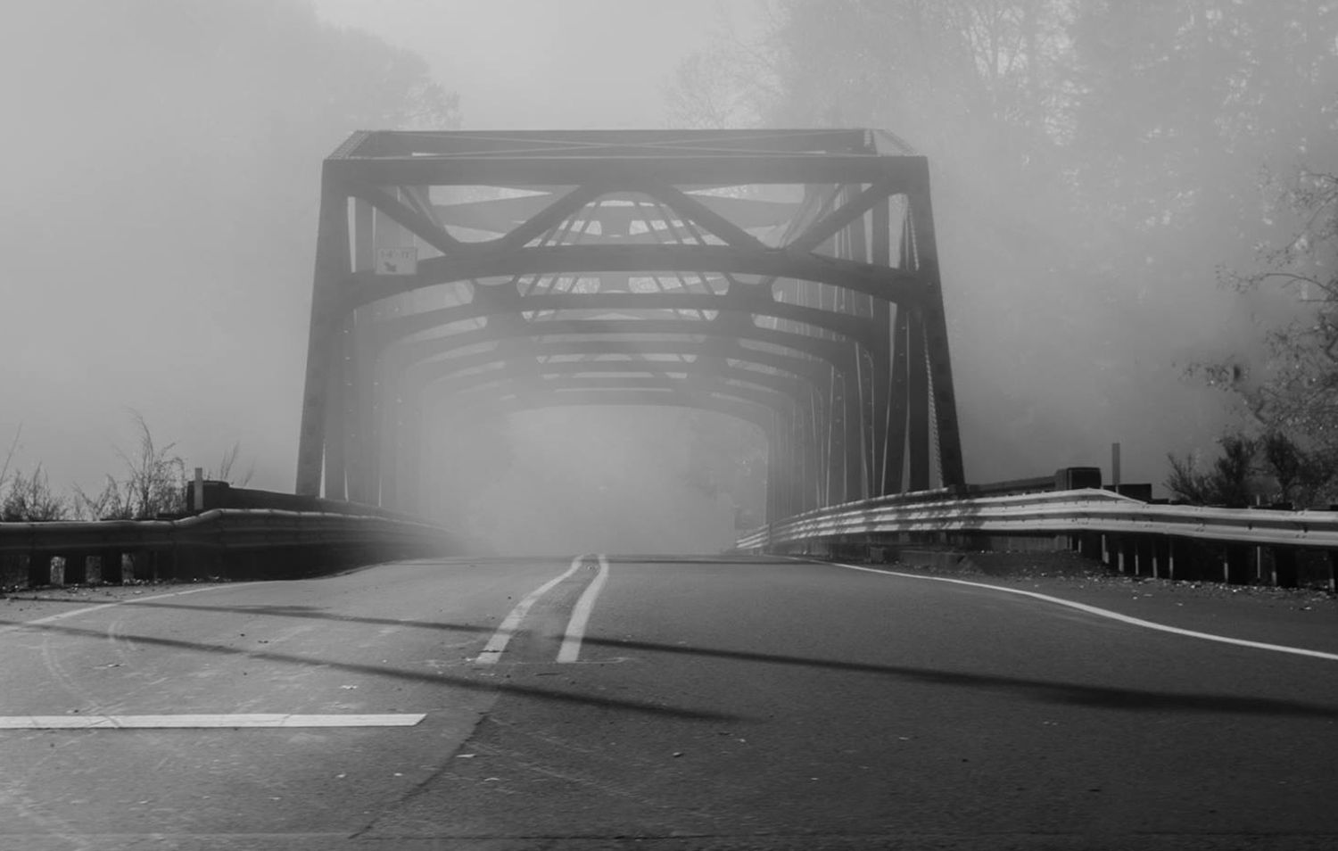 Steel bridge structure disappearing into thick fog on a rural highway.