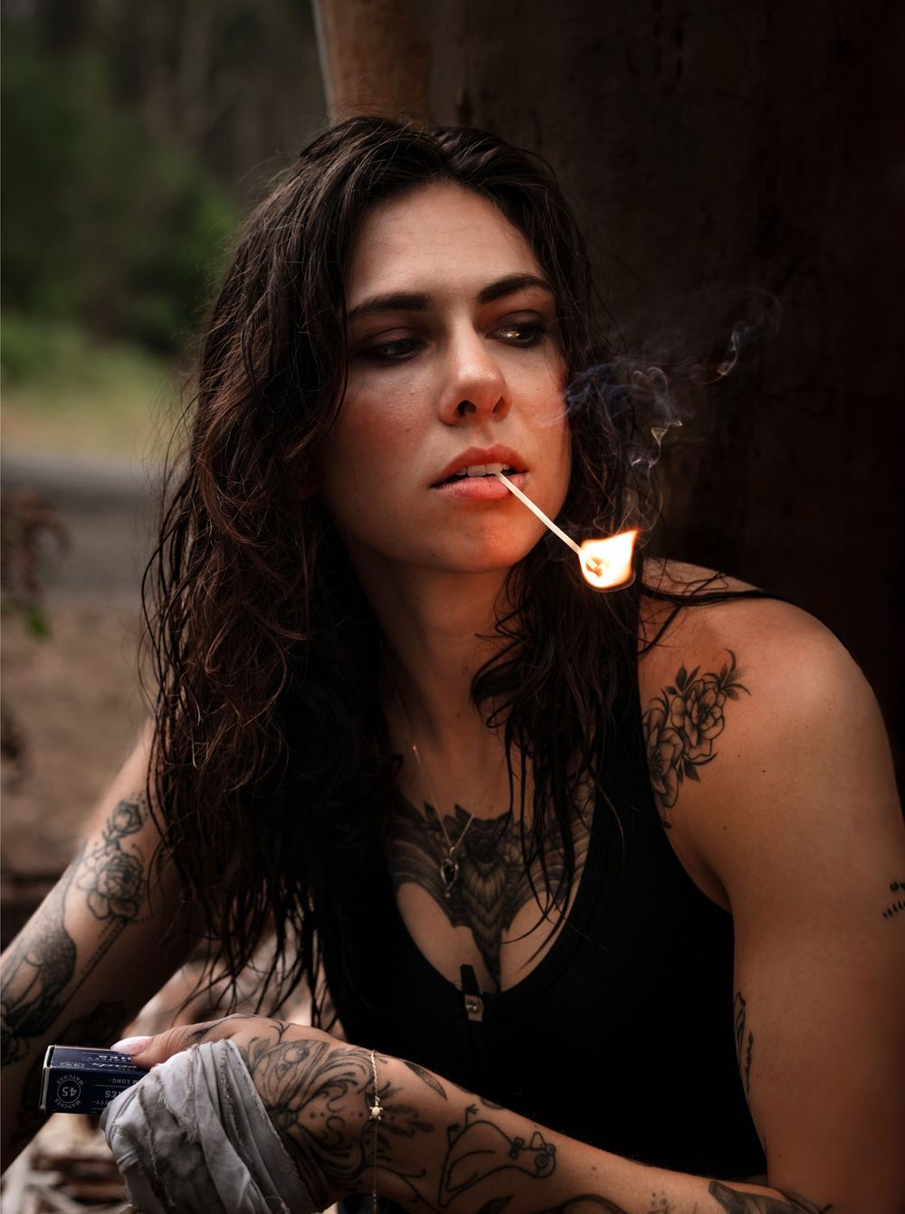Moody portrait with lit match and smoke in dark atmospheric setting.