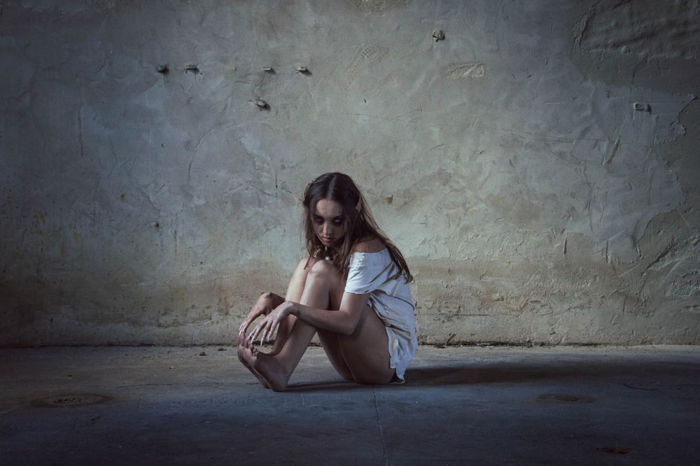 Moody atmospheric portrait of person sitting alone in dark concrete space showing signs of distress.