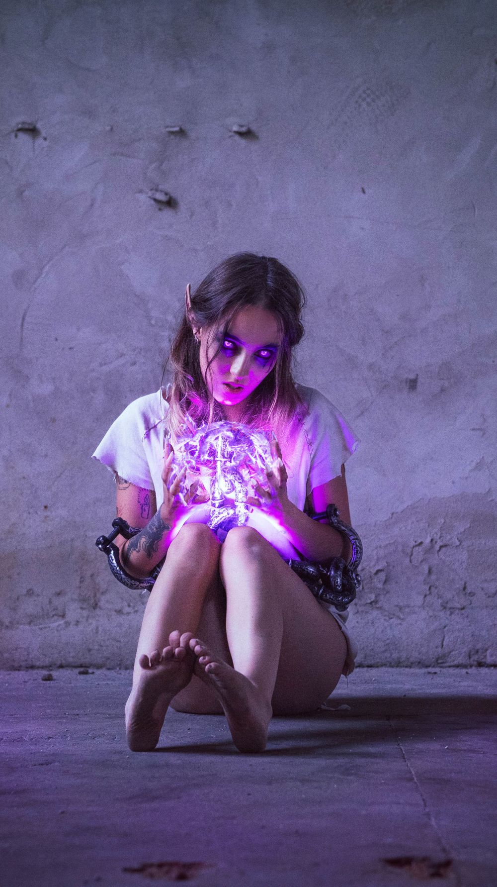 Sinister figure holding glowing purple light in dimly lit industrial setting.