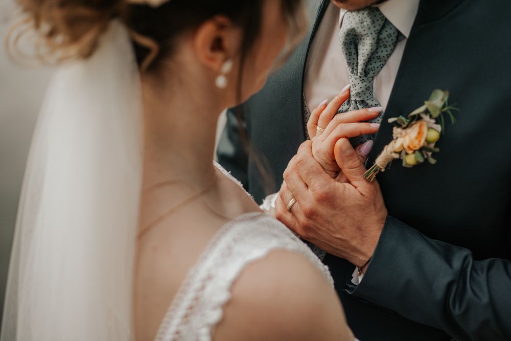 Bride and groom holding hands at wedding ceremony, showcasing elegant attire and floral boutonniere.