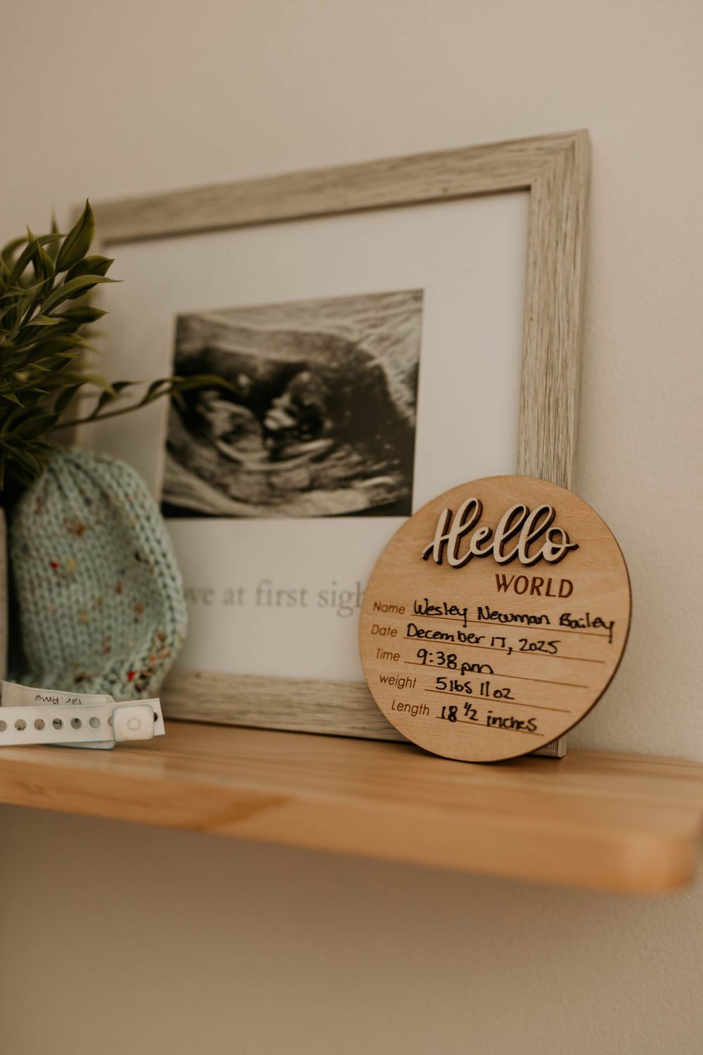 A wooden shelf displays ultrasound photos and a wooden 'Hello World' sign in a nursery setting.