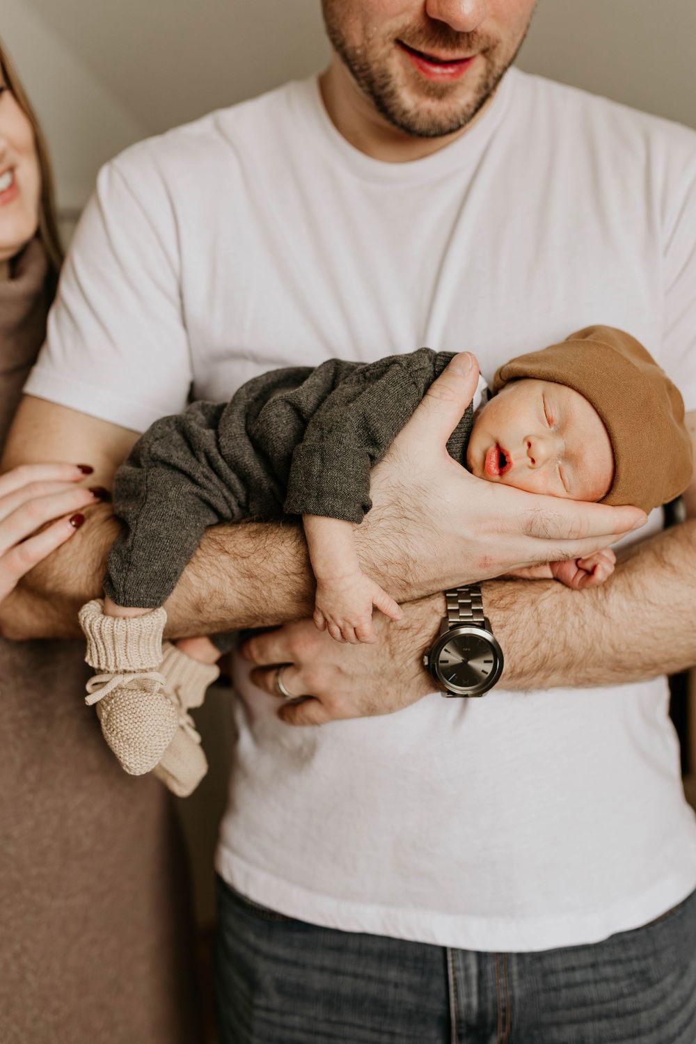 A series of lifestyle photos showing a parent cradling a sleeping newborn baby in a white t-shirt.