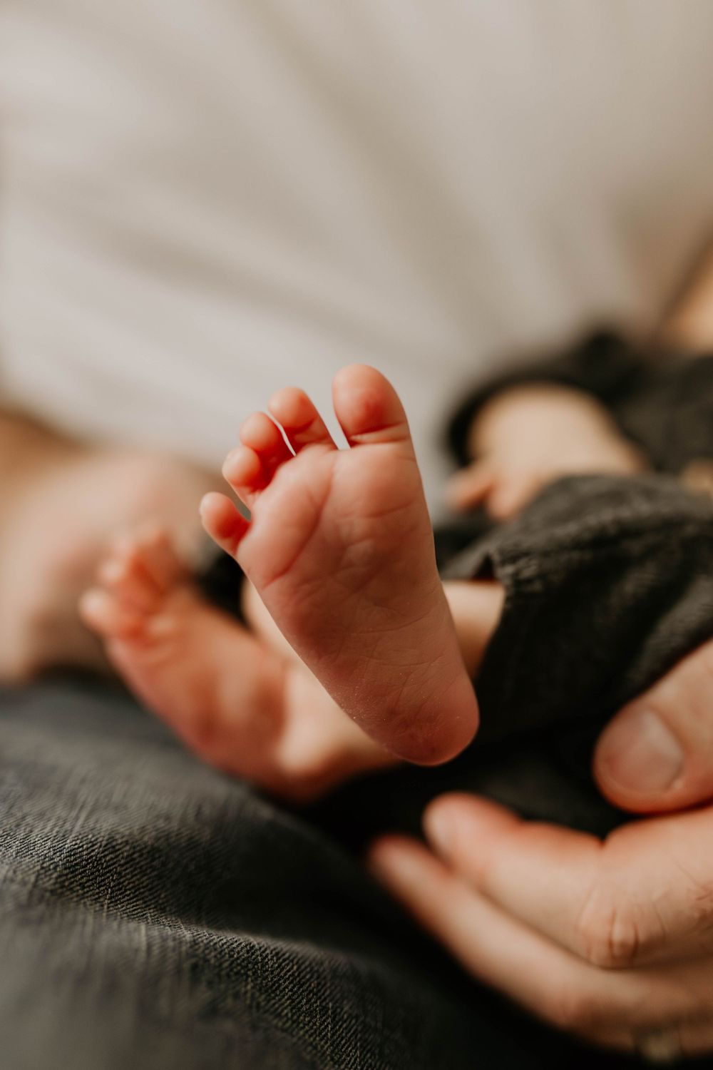 Close-up series of tiny baby feet resting on dark grey fabric in warm natural lighting.