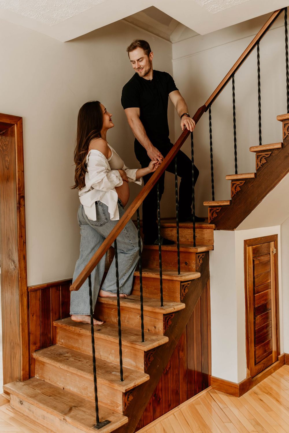 Couple shares intimate moment on wooden staircase in home with rustic wood paneling.