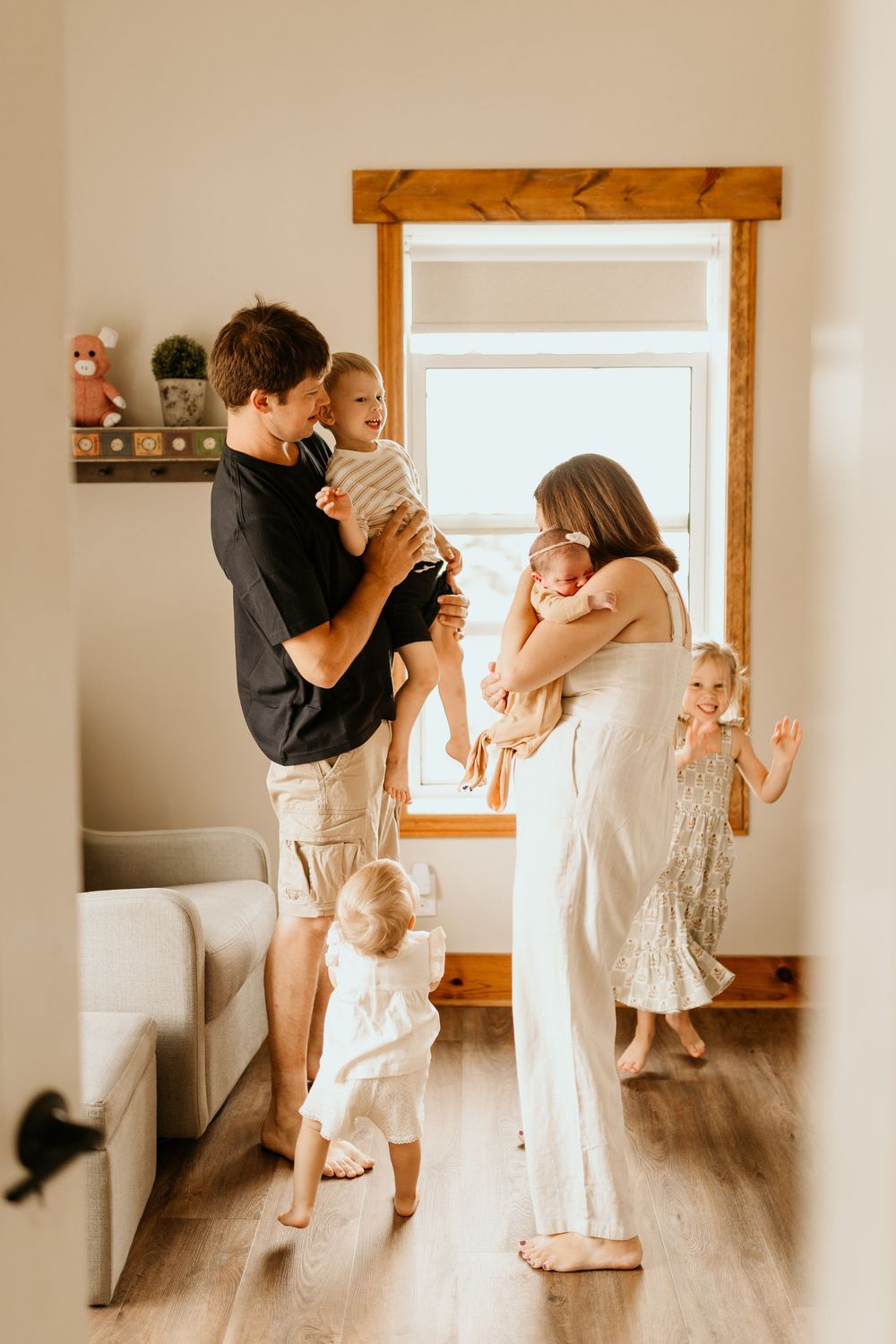 A family dances together in a bright sunlit room with wooden floors and white walls.