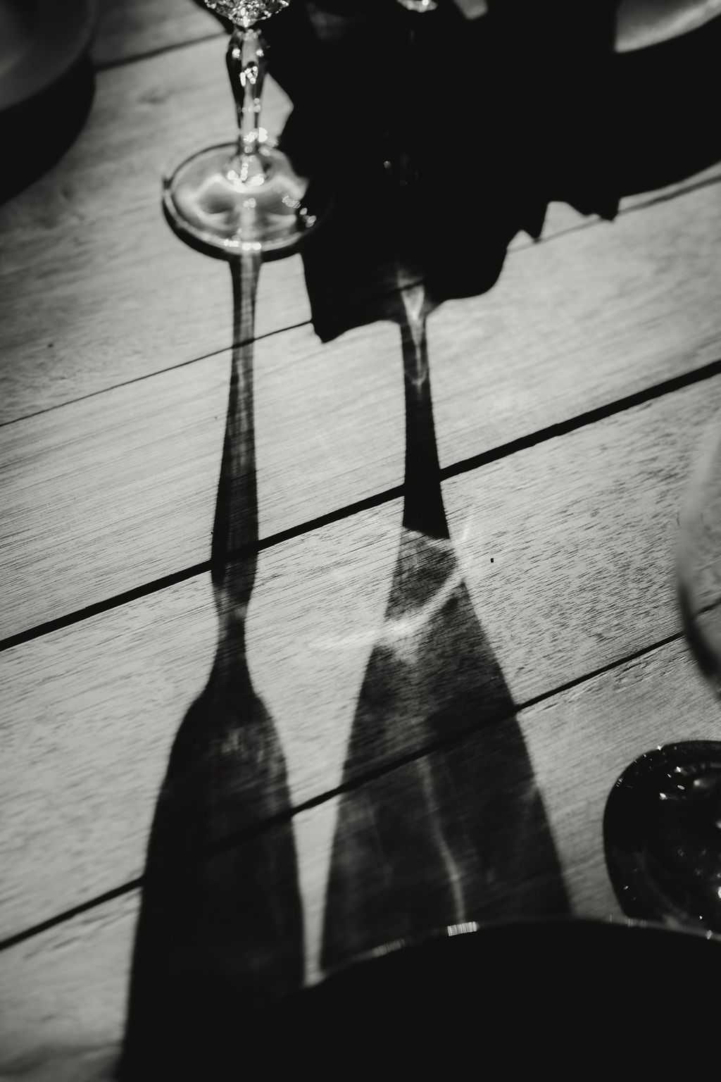 A black and white artistic photograph showing long shadows of wine glasses cast on a table. Intimate weddings Pretoria