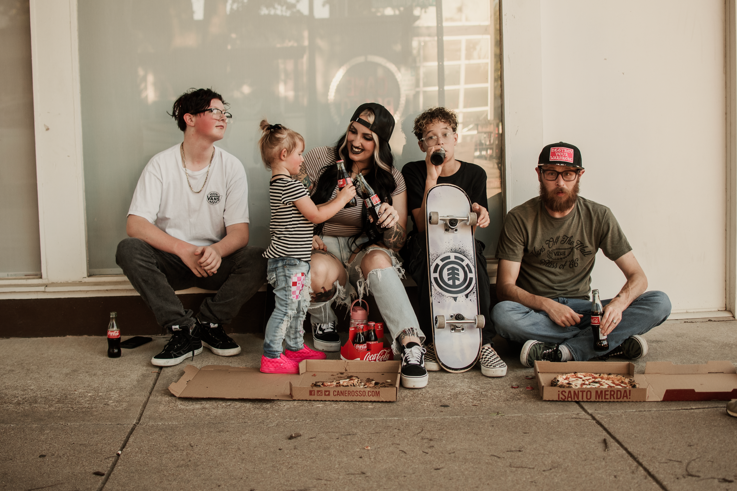 A group of people sitting on the ground against a wall, socializing and relaxing together.