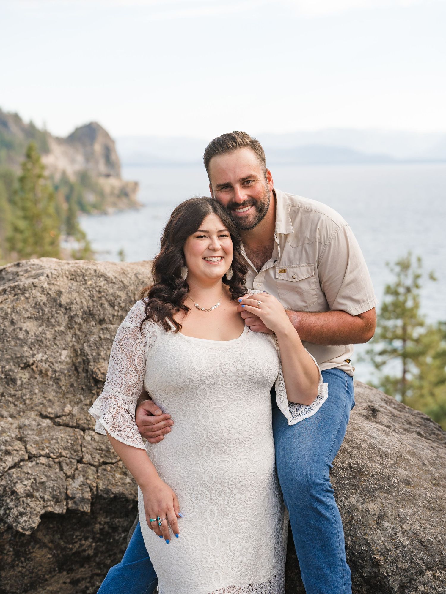 A couple poses together on a rocky outcrop overlooking Lake Tahoe scenic coastal landscape on a misty day.