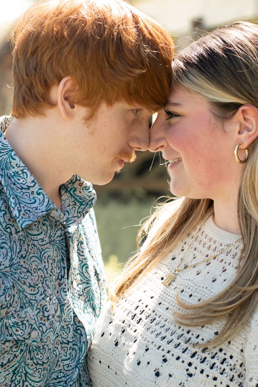 A romantic couple in a white dress and floral shirt share an intimate moment in golden sunlight.