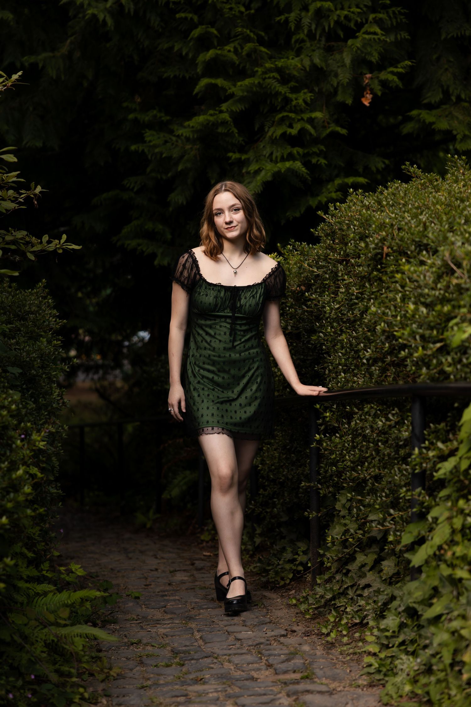 A dark green velvet dress is worn while walking along a garden path surrounded by lush greenery.