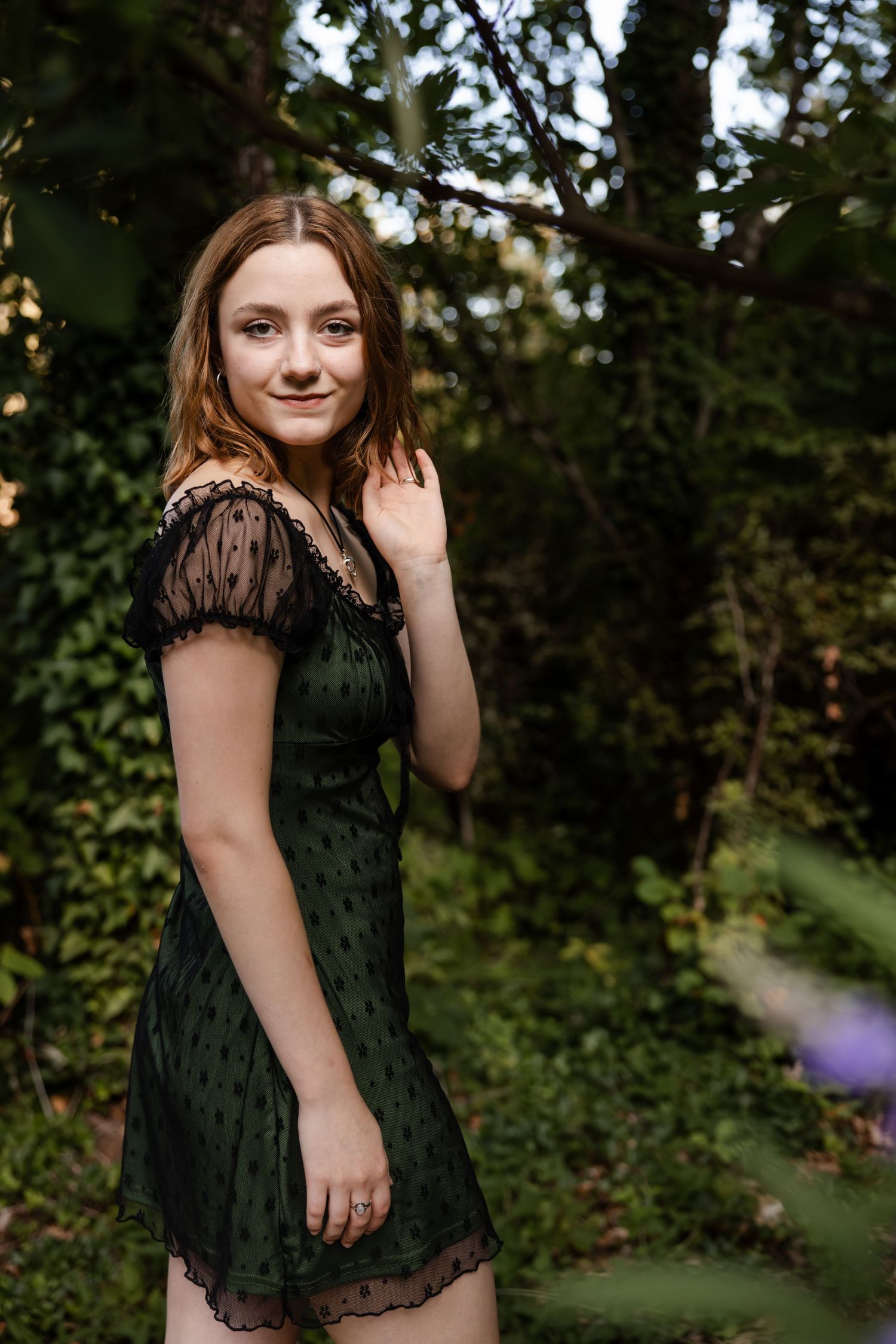 A graceful portrait in a lush garden setting, featuring a dark green lace dress with sheer cap sleeves.