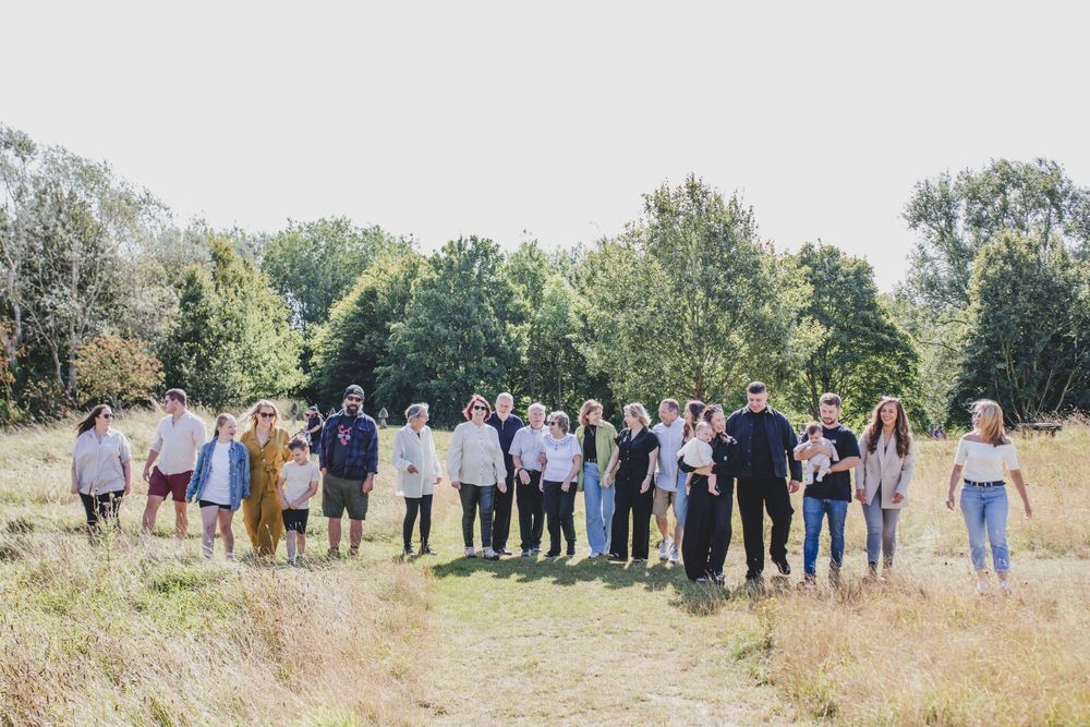 Extended family gathering outdoors in sunny field with trees in background.
Suffolk Family photos. Beckie Egan Photography.