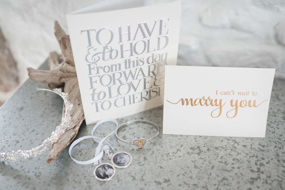Wedding details with white calligraphy cards reading 'To Have and To Hold' and 'Marry You' alongside silver rings on gray surface.