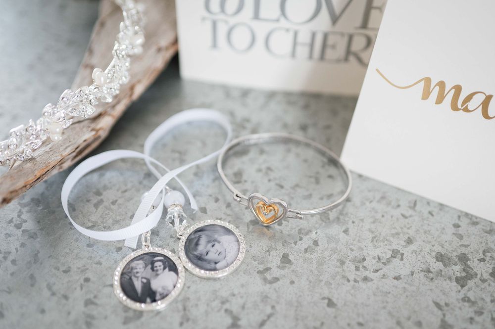 Delicate lace wedding details with silver jewelry, miniature photo charms and romantic decor elements on a gray surface.