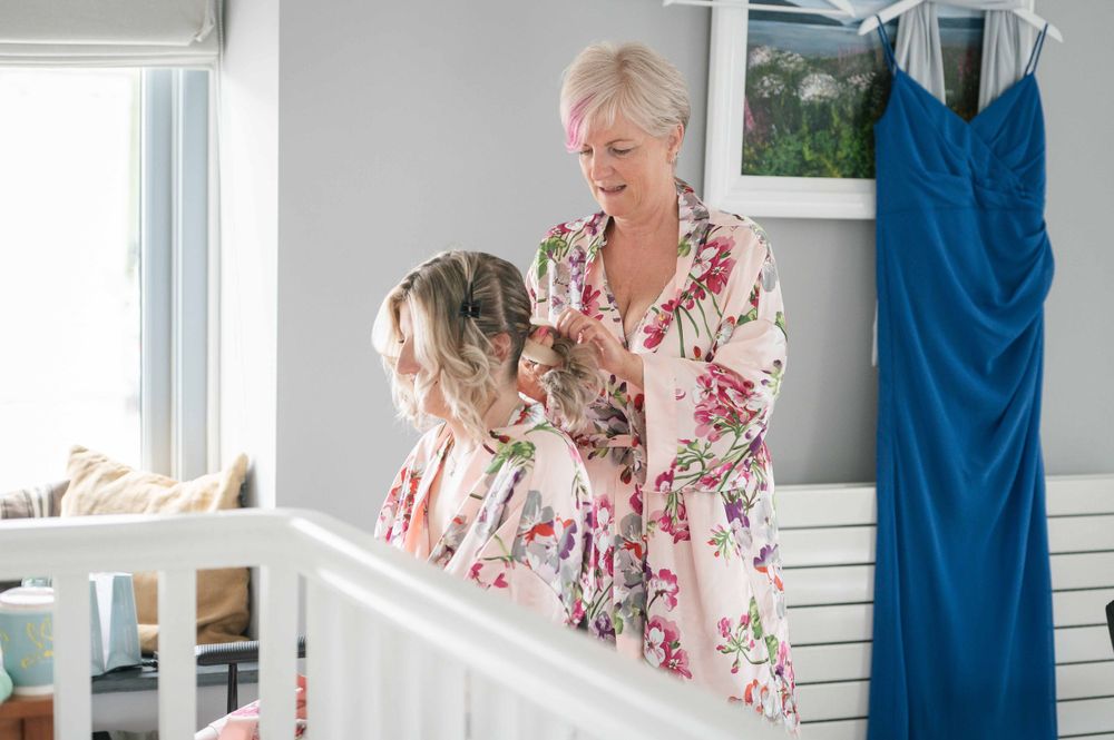 Two people wearing floral patterned robes are getting ready near a blue dress hanging on the wall.
