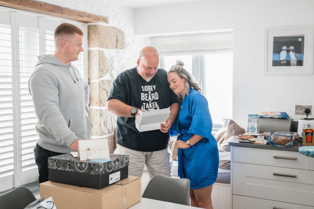Three people stand around a kitchen counter reviewing paperwork together while working on a project.