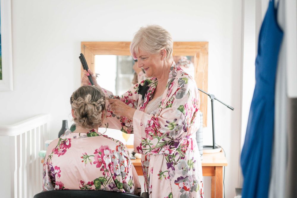 Person wearing a pink floral robe grooms a gray cat on a grooming table in a bright sunlit room.