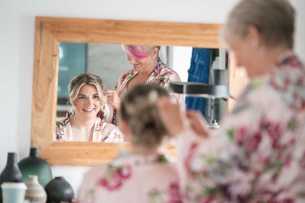 Reflection of someone smiling in a vanity mirror while getting ready with makeup products visible.