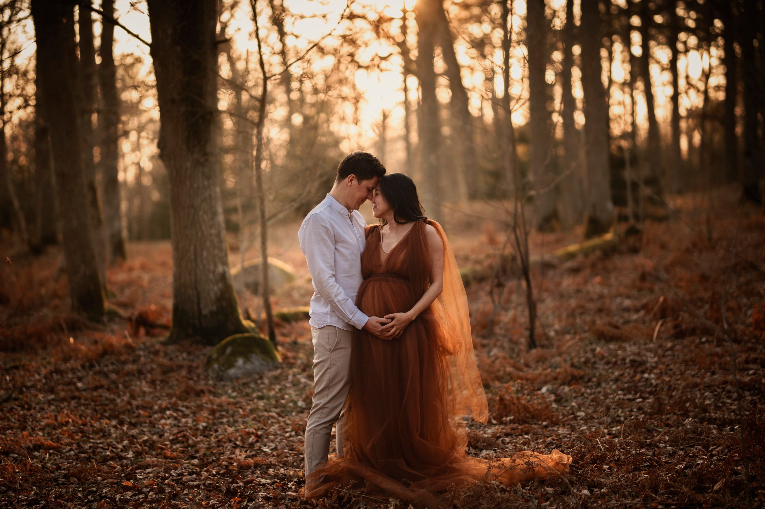 A romantic couple embraces in a sunlit autumn forest with golden light filtering through the trees during sunset.