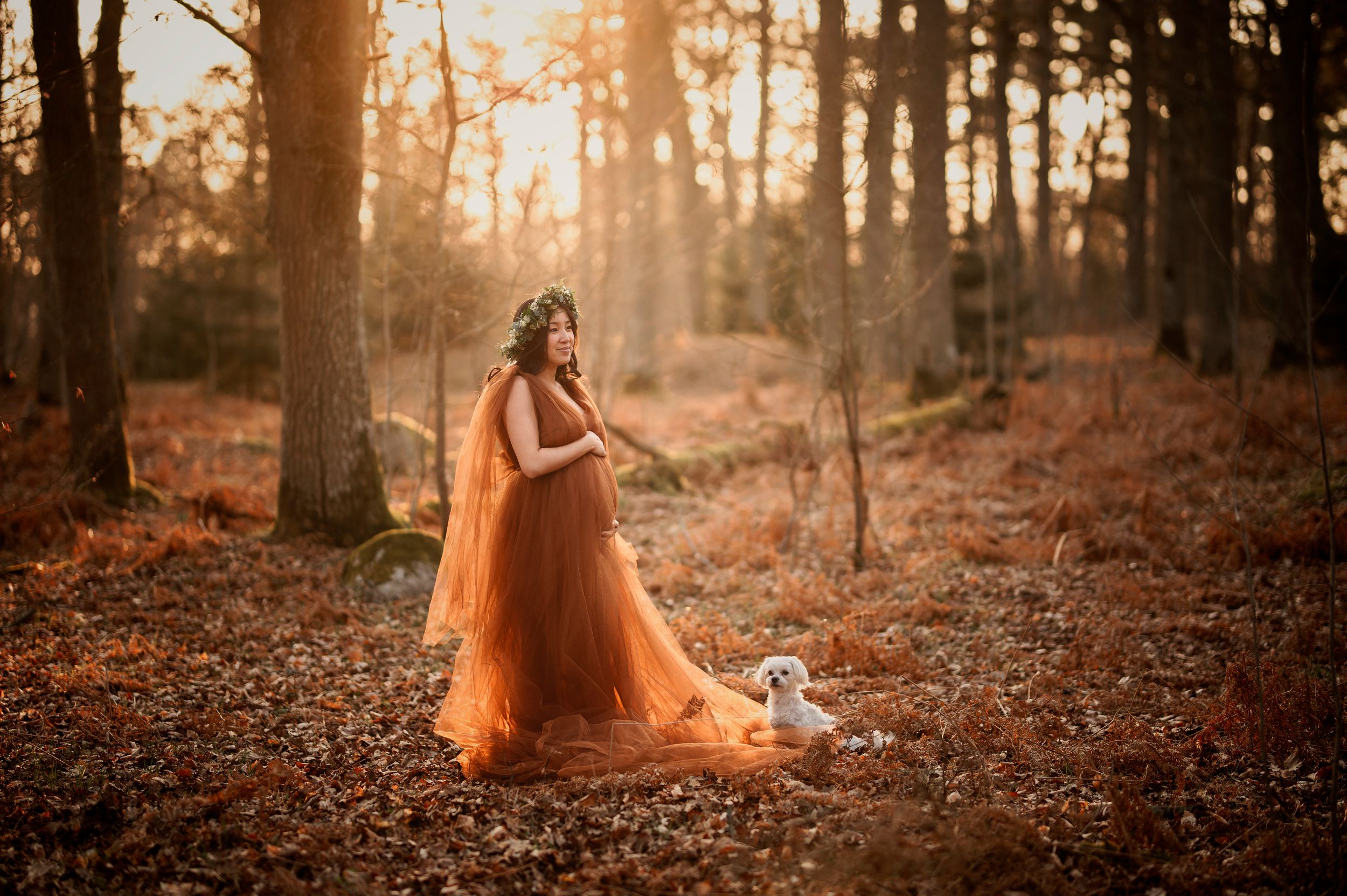 A flowing orange dress catches golden sunlight in an autumn forest during sunset.