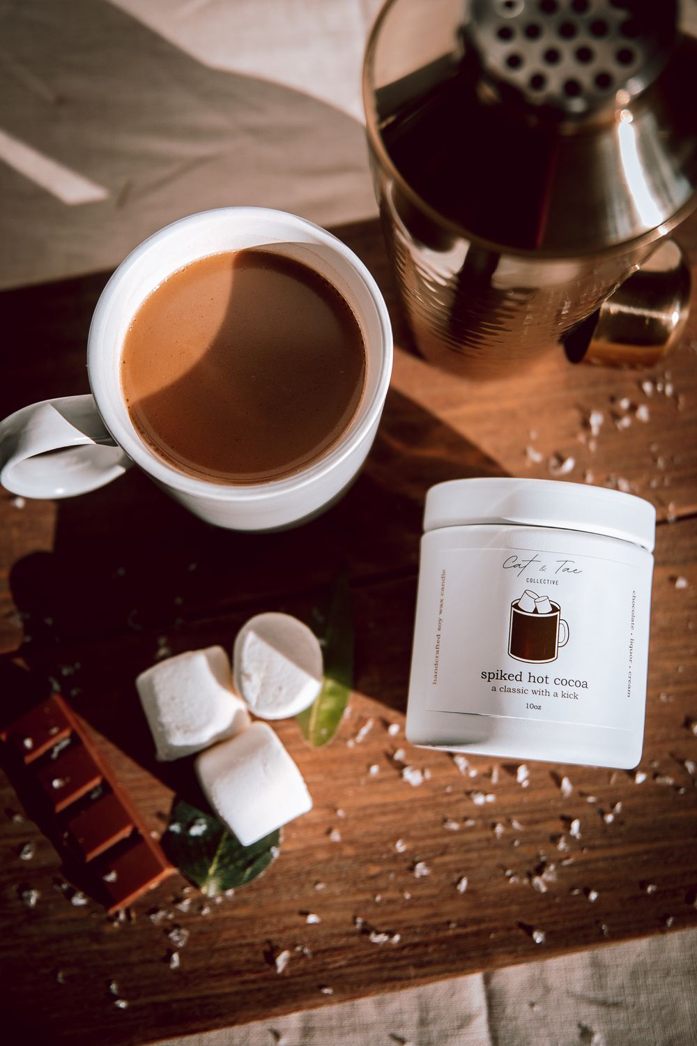 Overhead shot of coffee cup, marshmallows and white canister on wooden surface with natural lighting.