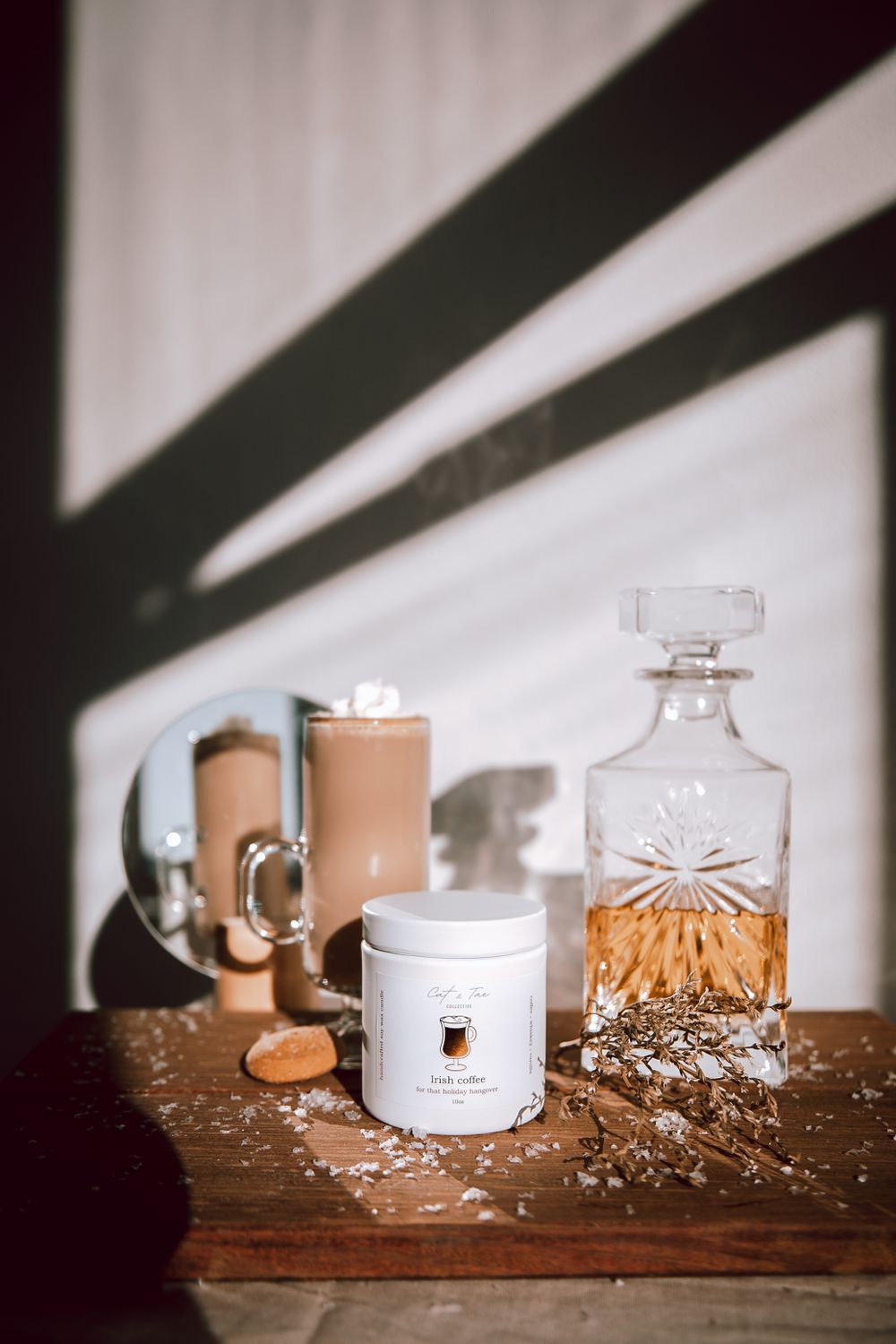 Aesthetic still life with coffee mug, crystal decanter, and white canister arranged on wooden surface with dramatic shadows.