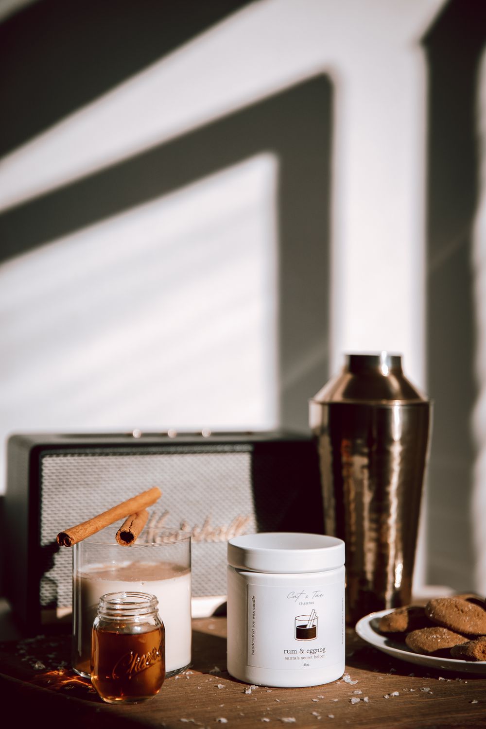 Moody coffee setup with cocktail shaker, mason jar, and cookies arranged with striking window shadows.
