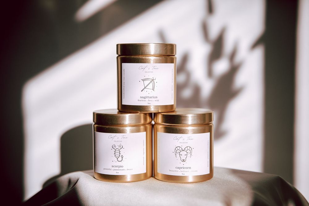 Three minimalist candle jars with gold lids arranged against a white wall with dramatic shadows.