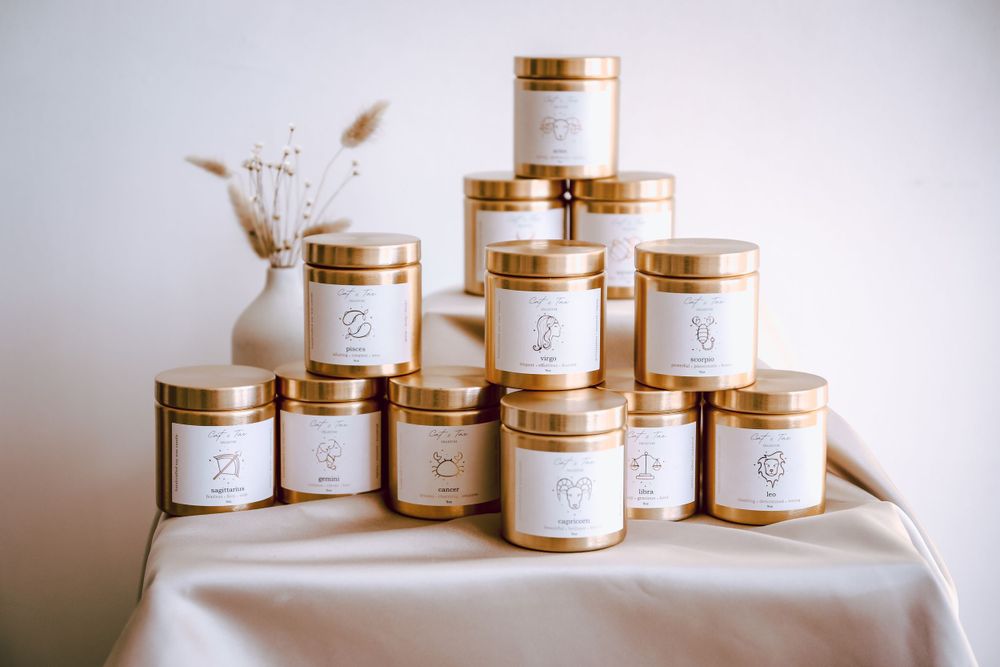 Collection of elegant gold-lidded candle jars stacked in pyramid formation on white fabric.