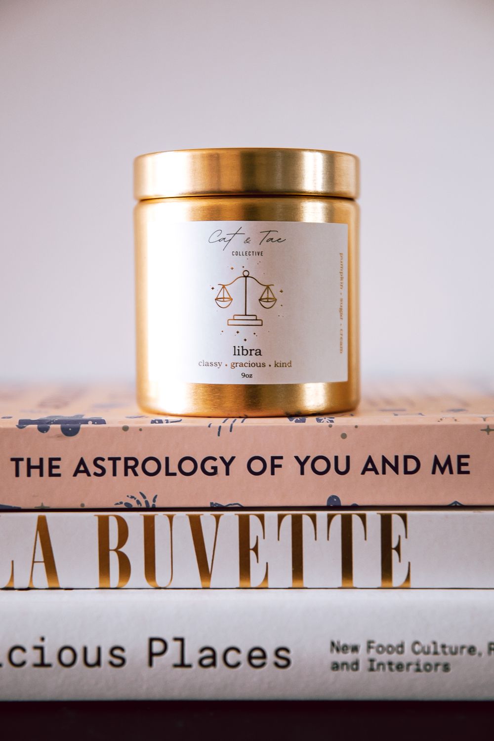 Astrology-themed candle displayed on stack of lifestyle books including 'The Astrology of You and Me'.