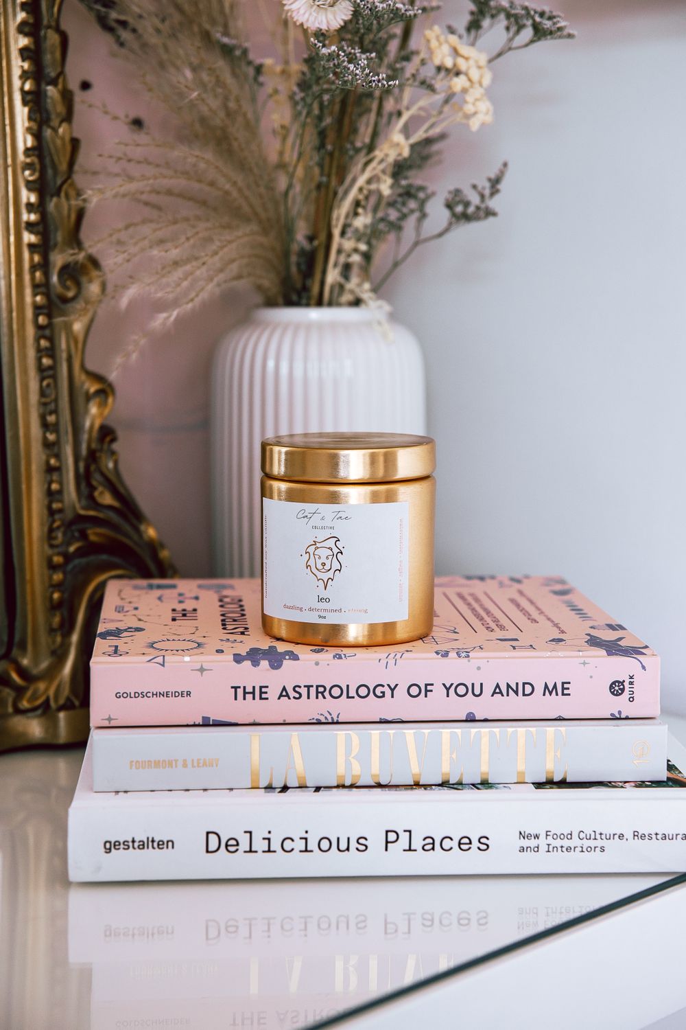 Elegant vignette featuring dried flowers, candle jar, and pink lifestyle books on white surface.