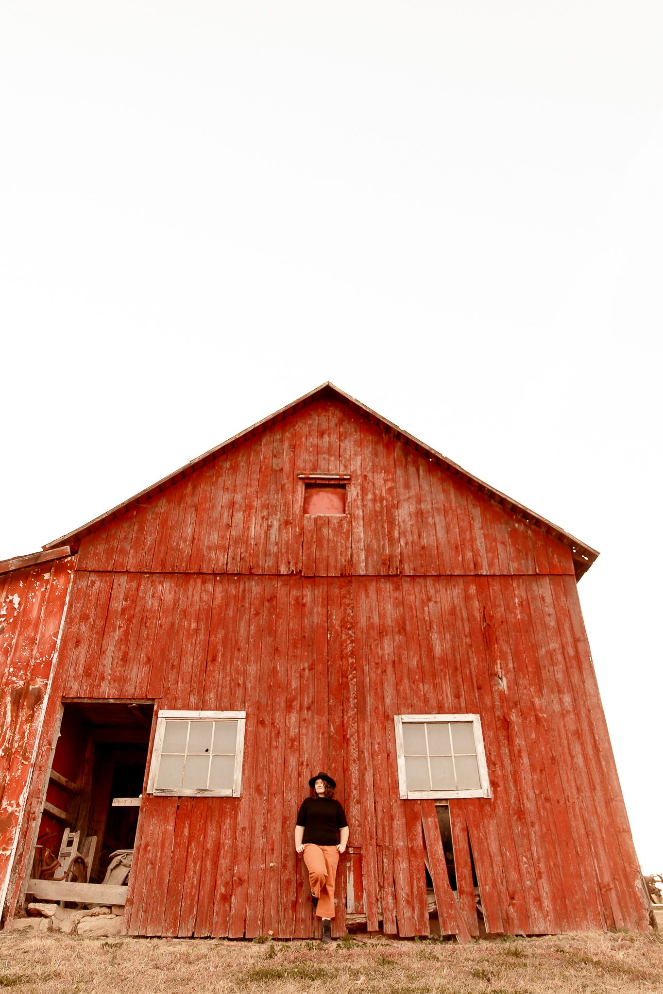 A rustic red wooden barn with two windows and an open doorway stands against a white background.