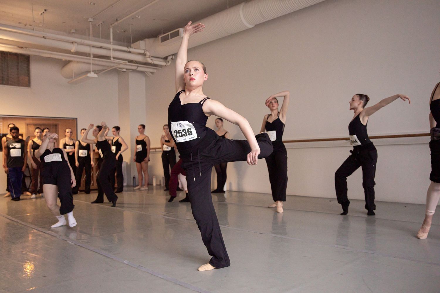 Group of dancers in black attire practicing choreography in bright studio space.
