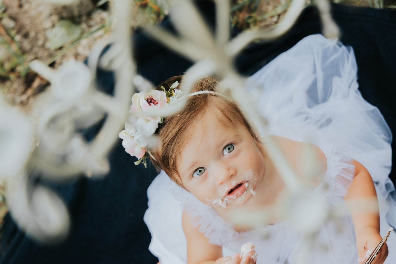 Close up of small child in white dress with floral crown looking up at hanging decorations.