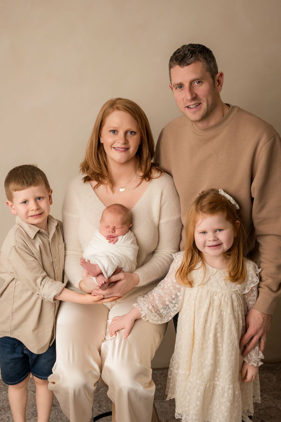 A family portrait series in neutral tones showing parents with children in cream and beige outfits against a simple timeless backdrop.