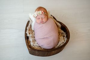 A series of newborn photography setup shots showing a wooden heart-shaped bowl with soft pink fabric and white decorations.