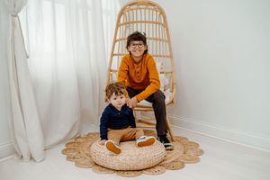 A rattan egg chair with white curtains and natural decor creates a cozy reading nook in a bright corner.