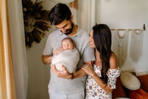 New parents posing together in a light and airy studio, mother, father, and newborn baby, smiling and snuggling