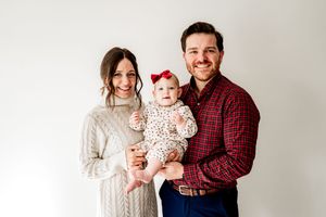 A family in coordinated winter outfits poses together for a holiday portrait session against a light background.