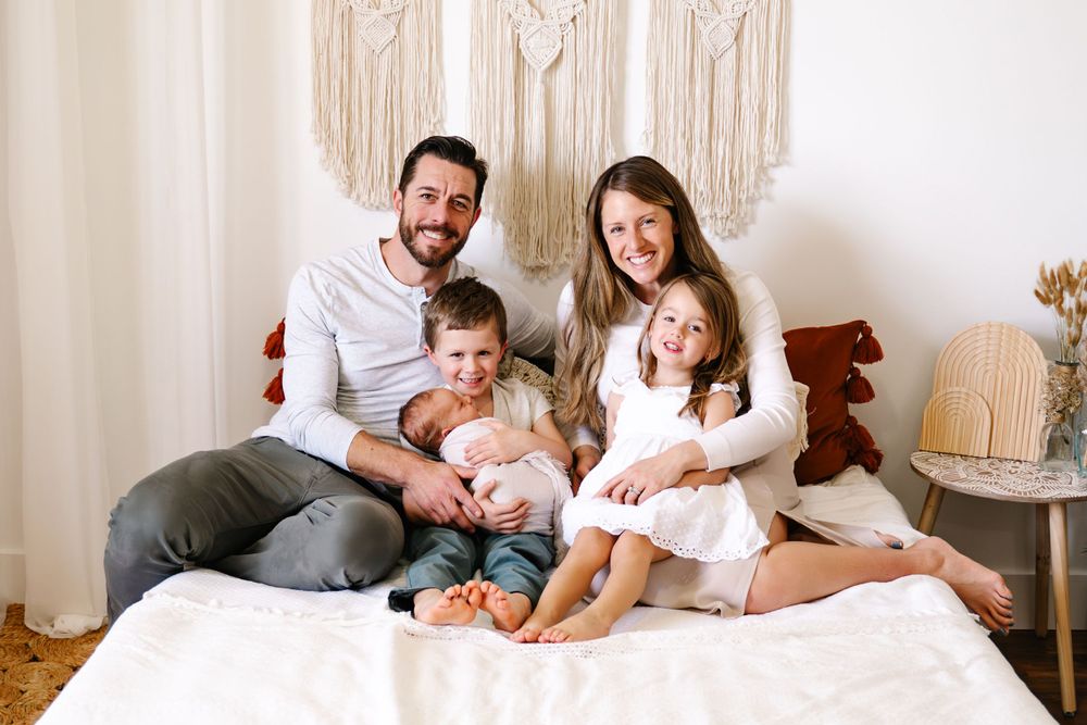 Family of five posing together in a light and airy studio, mother, father, and three children, smiling and snuggling