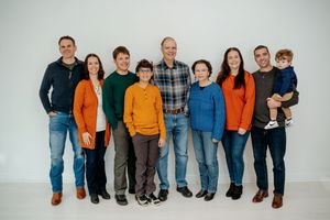 A group of people wearing coordinated orange and blue casual outfits sit together on a white backdrop.