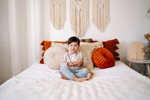 Toddler boy wearing a light blue button-up shirt and jeans, smiling for a photoshoot in a boho studio.