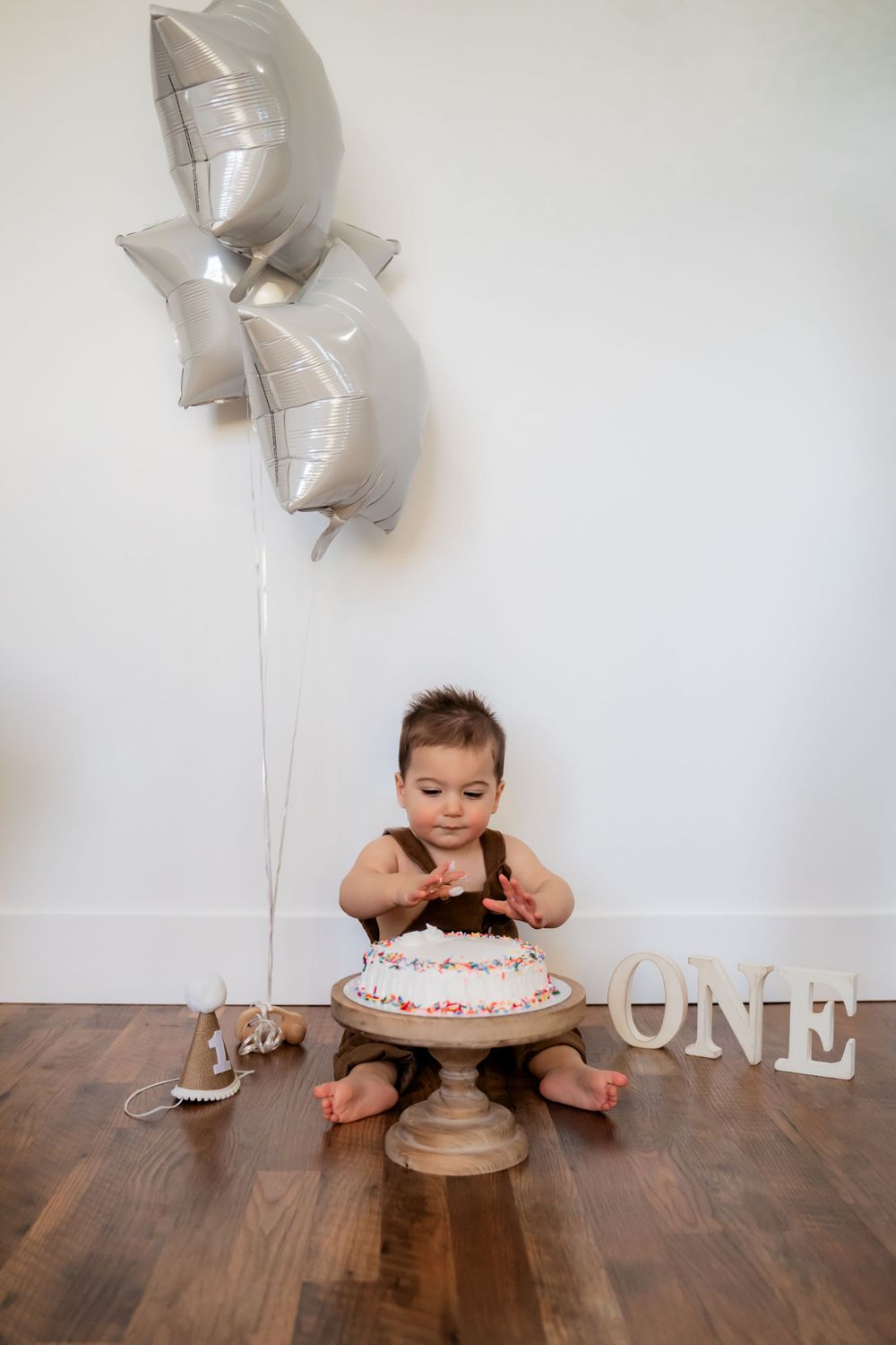 Toddler boy wearing brown overalls for a smash cake milestone first birthday session.