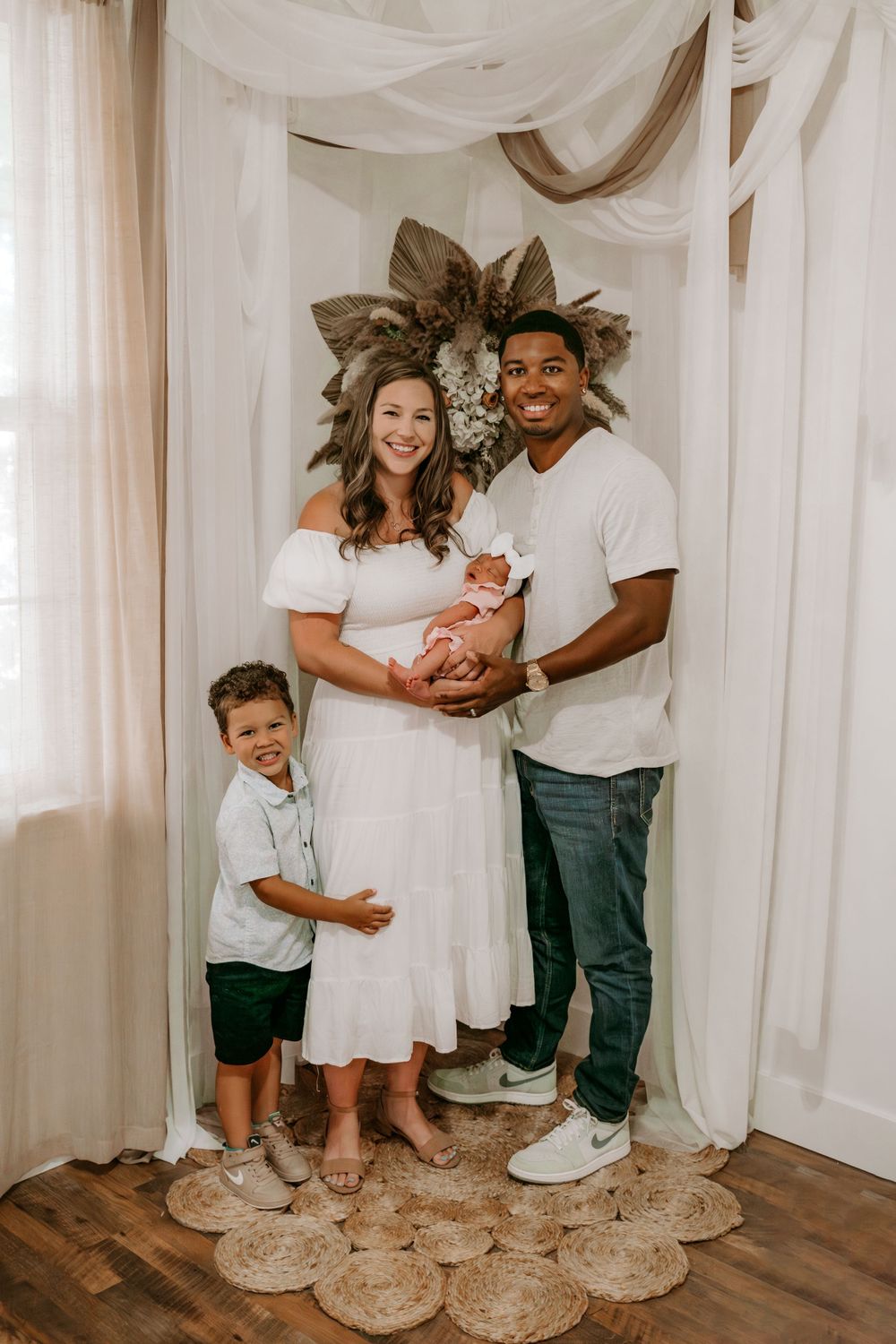 Family of four posing together in a light and airy studio, mother, father, and children, smiling and snuggling