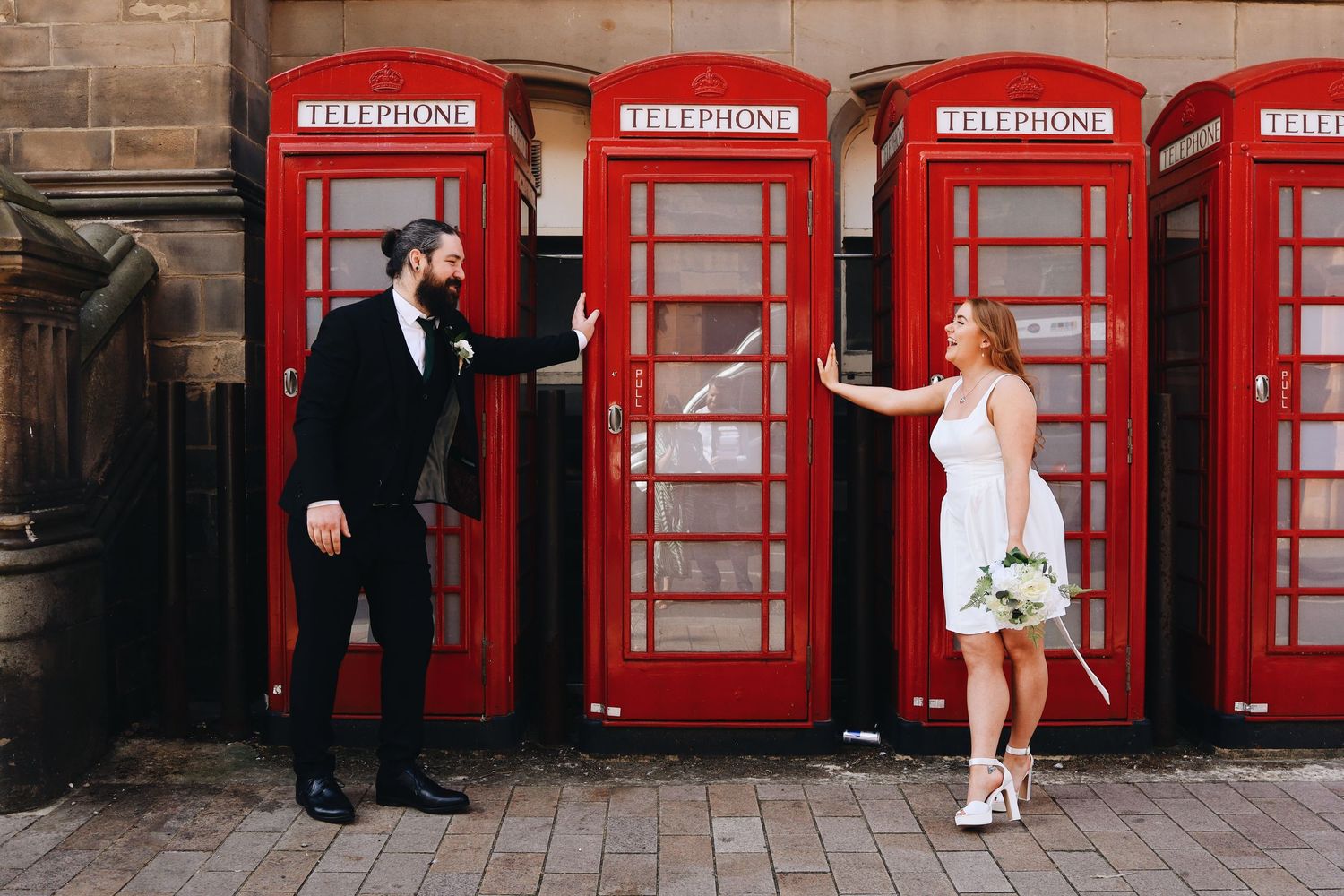 Row of classic red British telephone boxes against stone building facade.