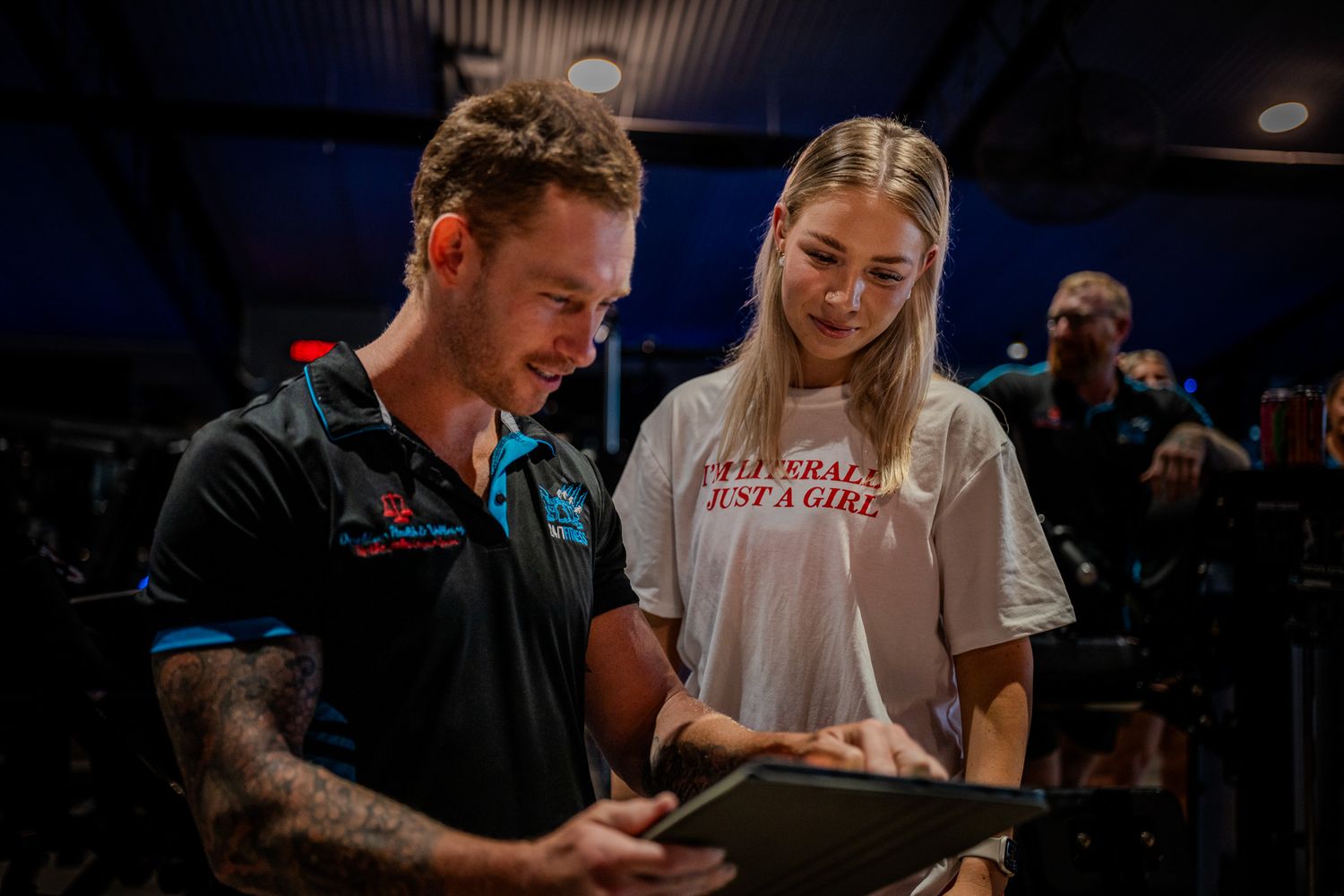 Two people look down at a digital device while sharing a moment together in a dimly lit indoor setting.