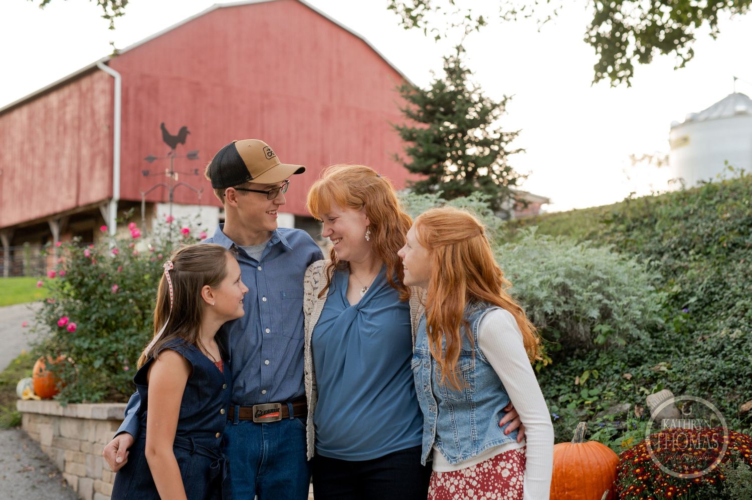 Candid family moment captured outside a red barn with pumpkins and greenery.