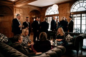 A group of people socializing in an elegant wood-paneled room with arched windows and plush seating.